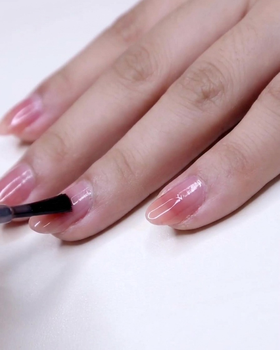 Vue rapprochée dun pinceau appliquant du vernis rose du centre vers la pointe dun ongle.