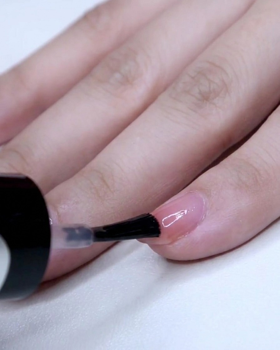 Un pinceau à ongles appliquant une couche concentrée de vernis rose sur la pointe dun petit doigt.