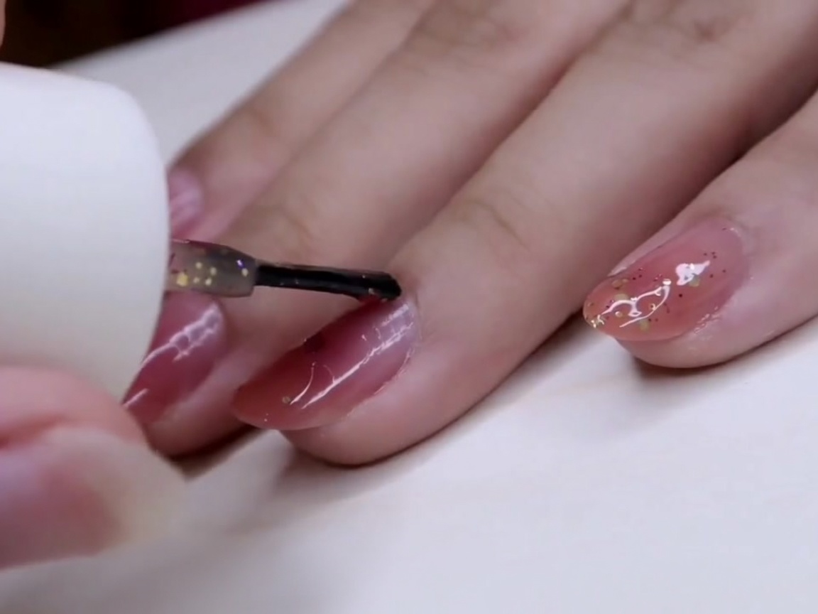 Un pinceau étalant du vernis à paillettes sur le majeur, en concentrant les flocons près de la pointe.
