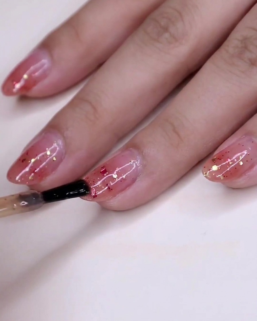 Une vue de la main avec du vernis à paillettes humide se fixant sur les ongles sur la base dégradée rose.
