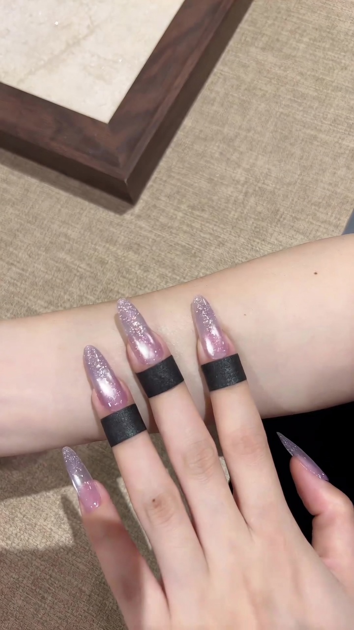 Ongles longs en forme damande présentant une transition sophistiquée entre une base œil de chat violette translucide et un bout aux paillettes scintillantes.