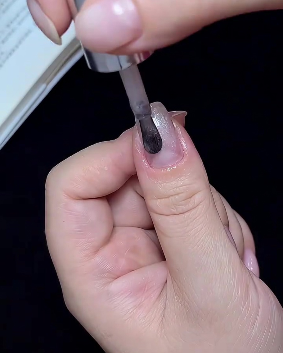 Un pinceau appliquant du vernis gel œil de chat blanc translucide sur un ongle.