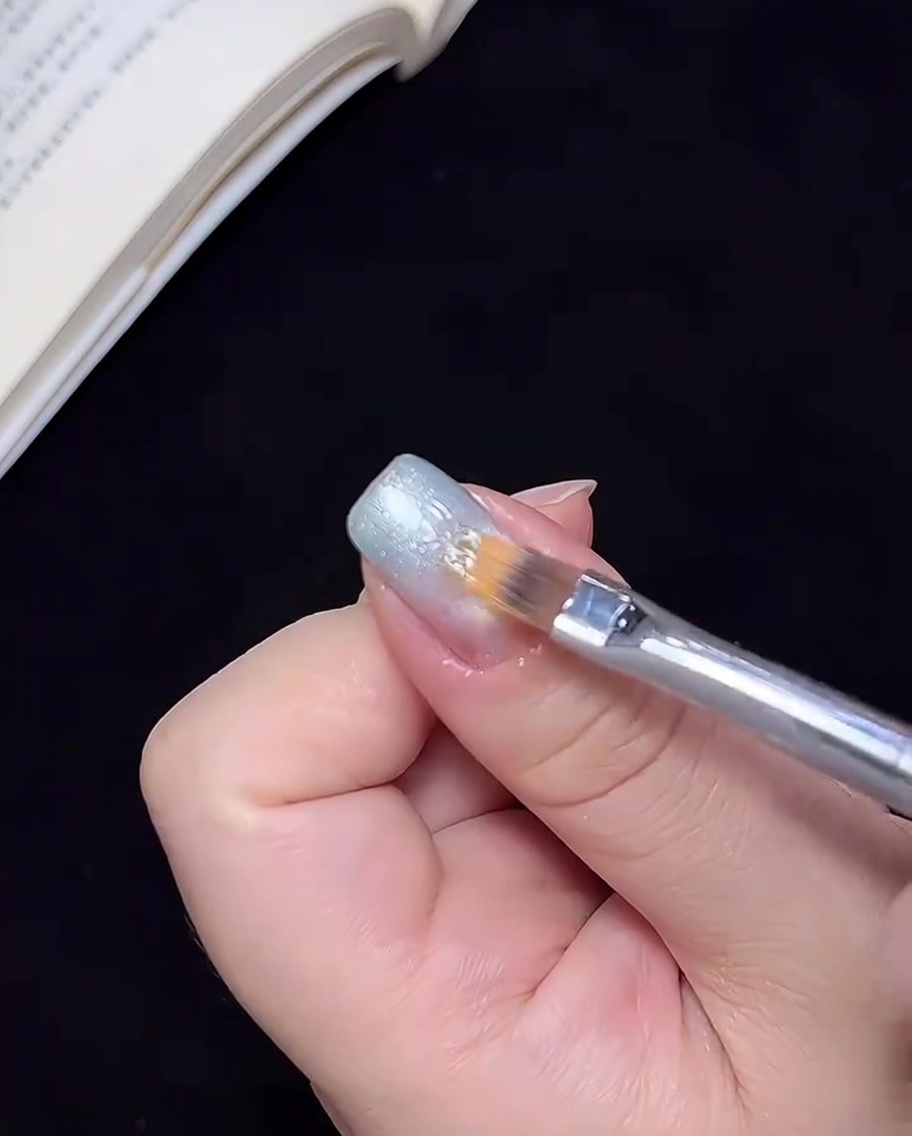 Un pinceau estompant le gel bleu vers le centre de longle pour créer une transition ombré.