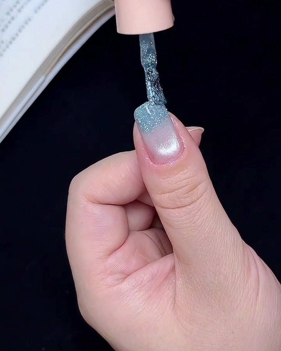 Un pinceau nail art appliquant du gel à paillettes bleues sur le bord de longle.
