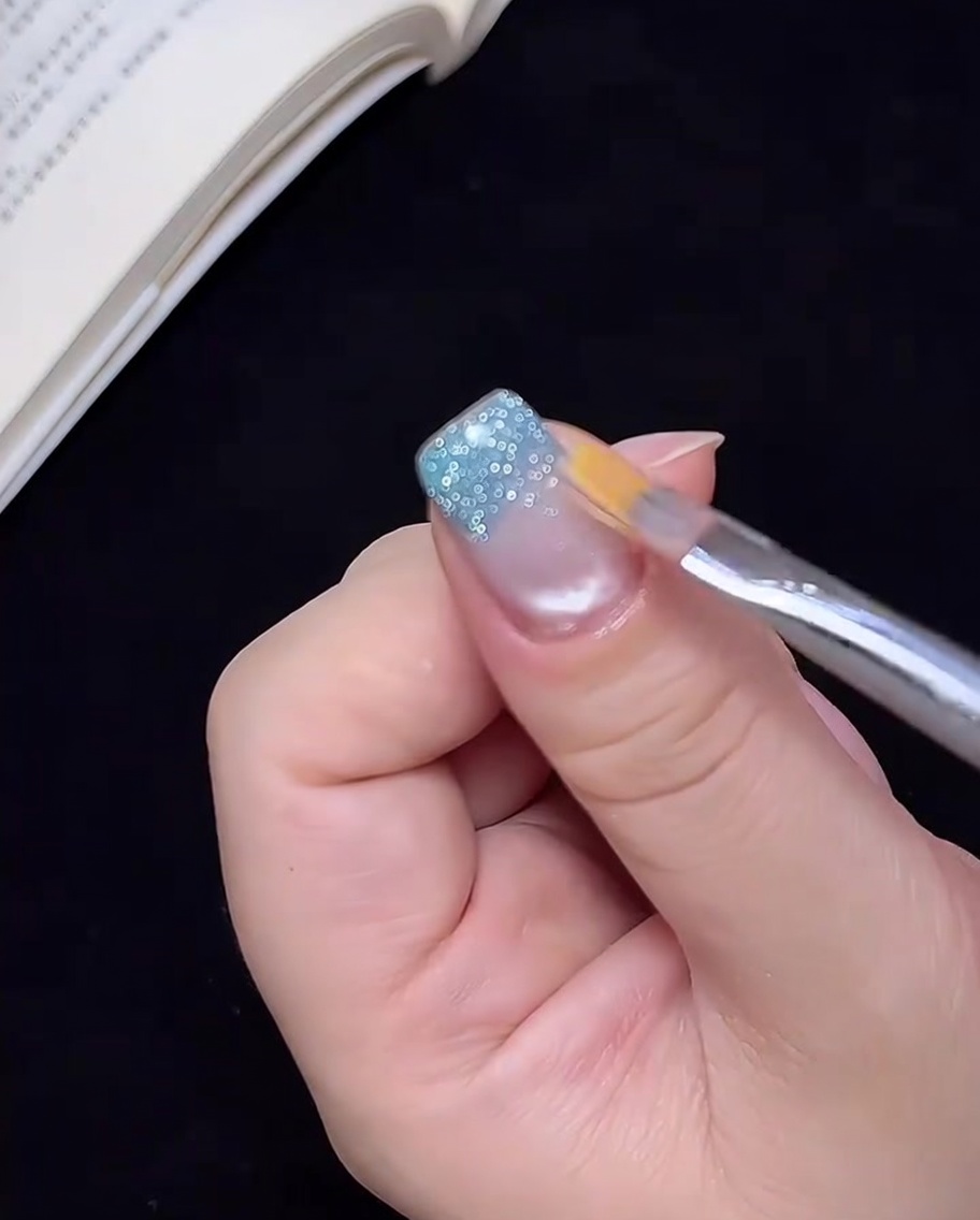 Un pinceau propre étirant légèrement les paillettes bleues vers le milieu de longle.
