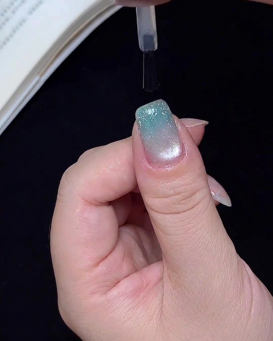 Un pinceau appliquant un top coat brillant transparent sur longle fini.
