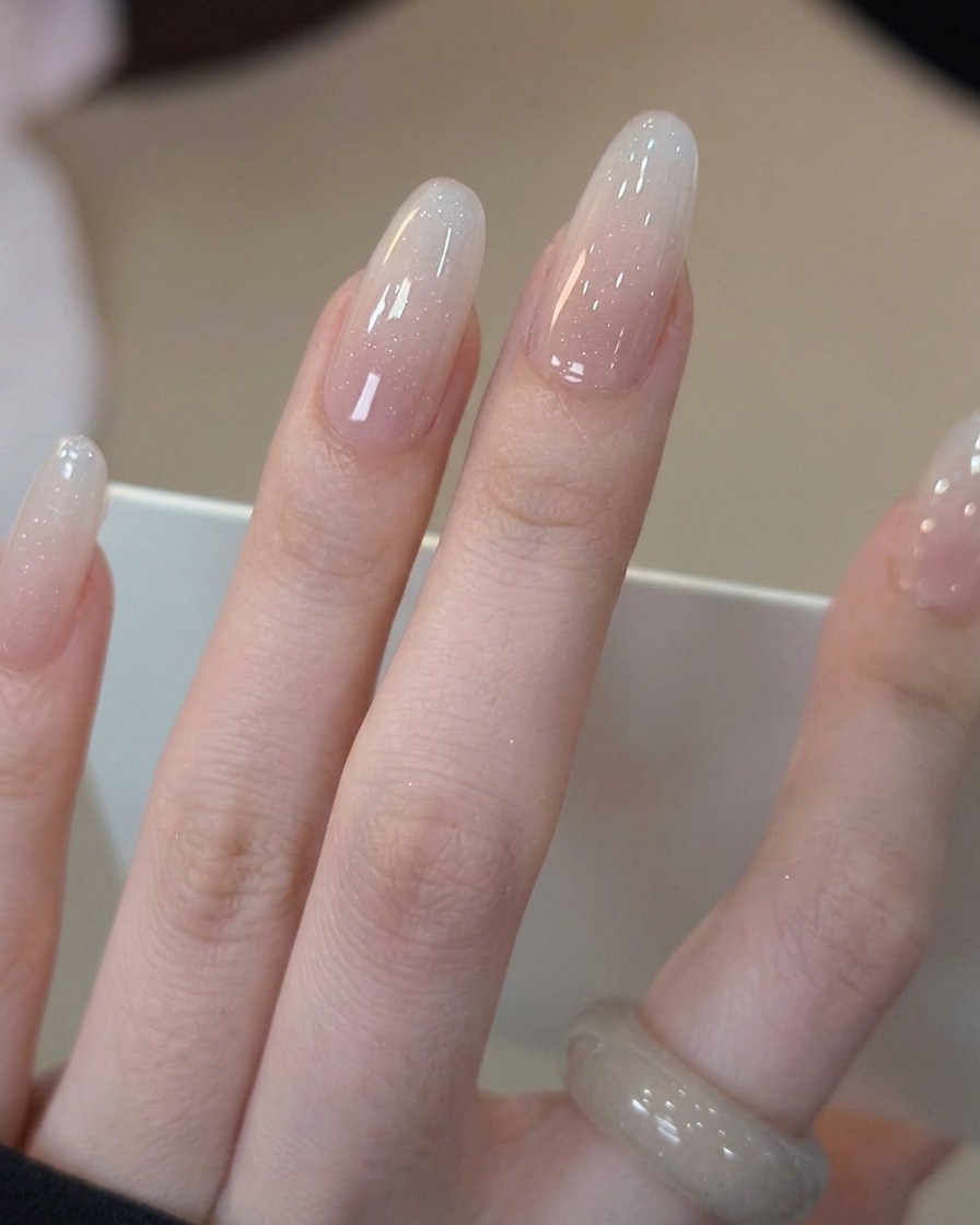 Un pinceau appliquant un top coat transparent brillant sur un ongle avec un dégradé blanc laiteux.