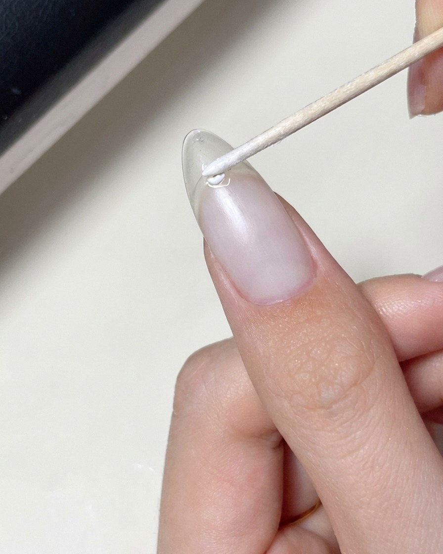 Un pinceau appliquant une couche de gel transparent sur un ongle déjà orné dun autocollant étoile.
