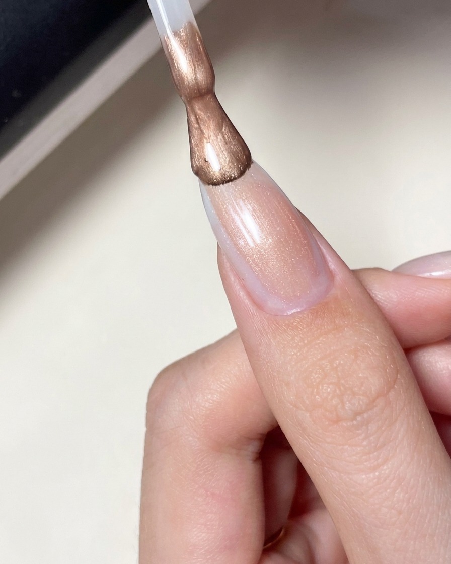 Un pinceau appliquant un vernis gel rose laiteux et transparent sur un ongle avec un motif détoile.