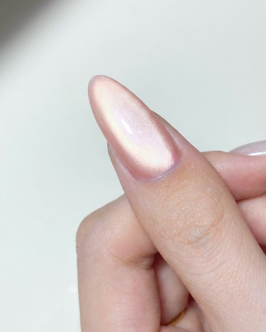 Un applicateur déposant de la poudre chrome aurore scintillante sur la surface dun ongle en gel catalysé.