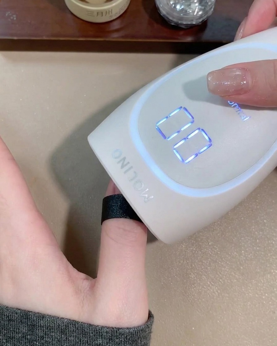 Une main placée dans une lampe à ongles portable blanche pour catalyser le gel.