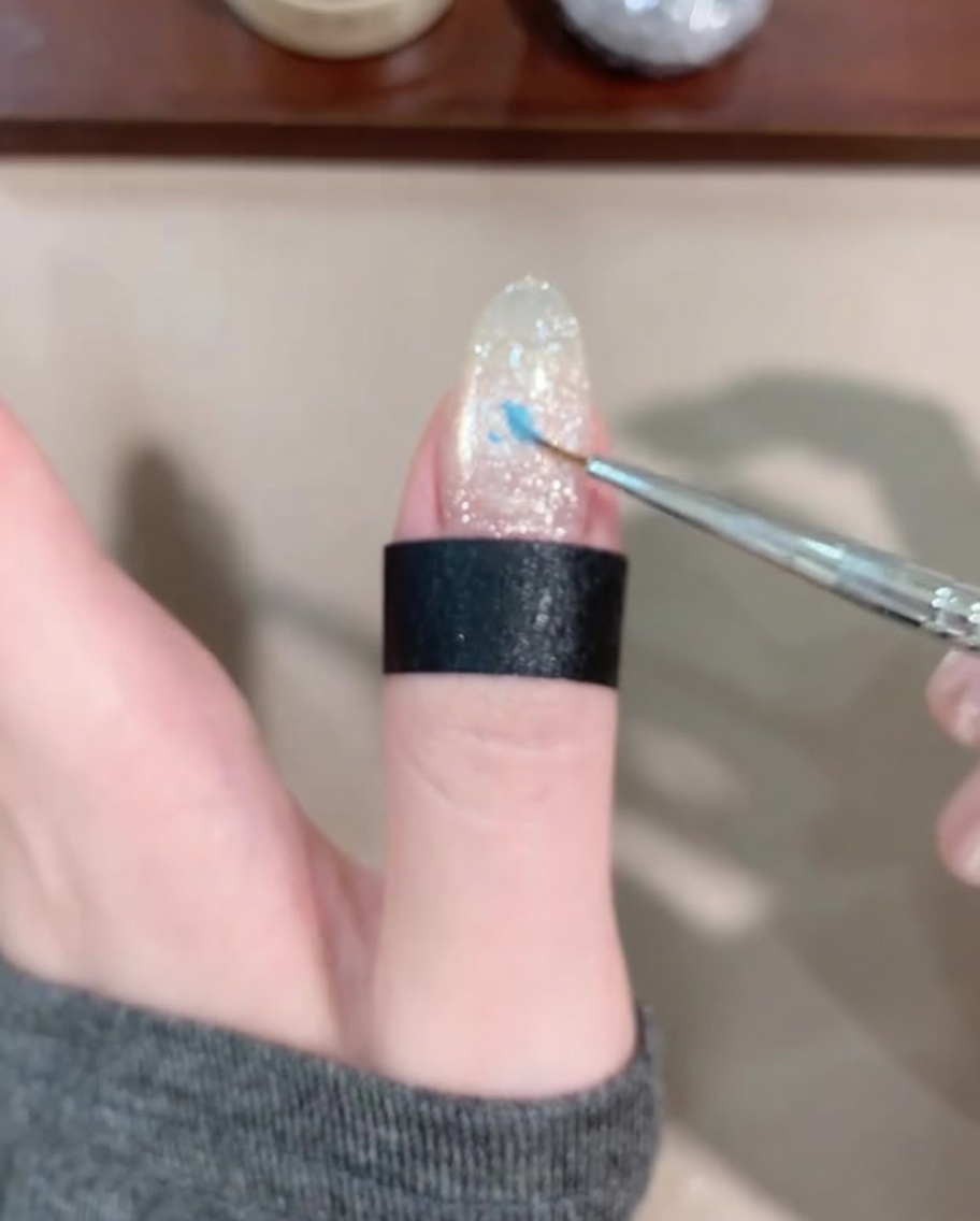Un pinceau fin appliquant une petite goutte de gel bleu au centre de longle.