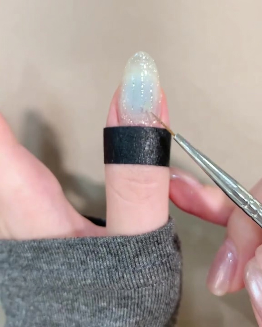 Une pince déposant une petite étoile dorée sur un ongle clair décoré.