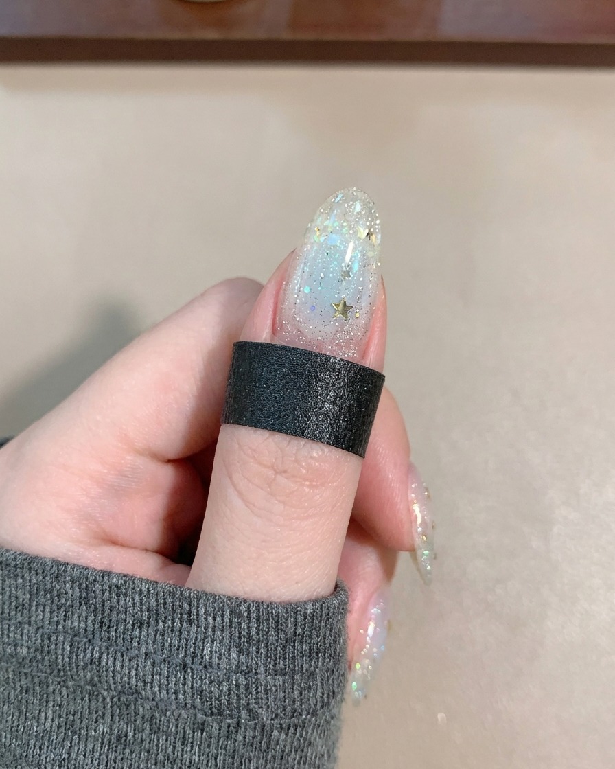 Un pinceau appliquant un top coat brillant sur un ongle décoré détoiles et de lignes.