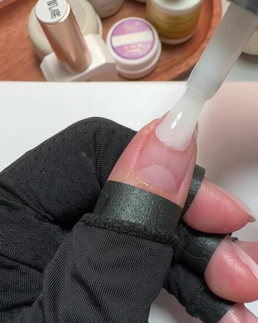 Gros plan dun pinceau appliquant du vernis gel blanc laiteux sur un ongle de pouce préparé.
