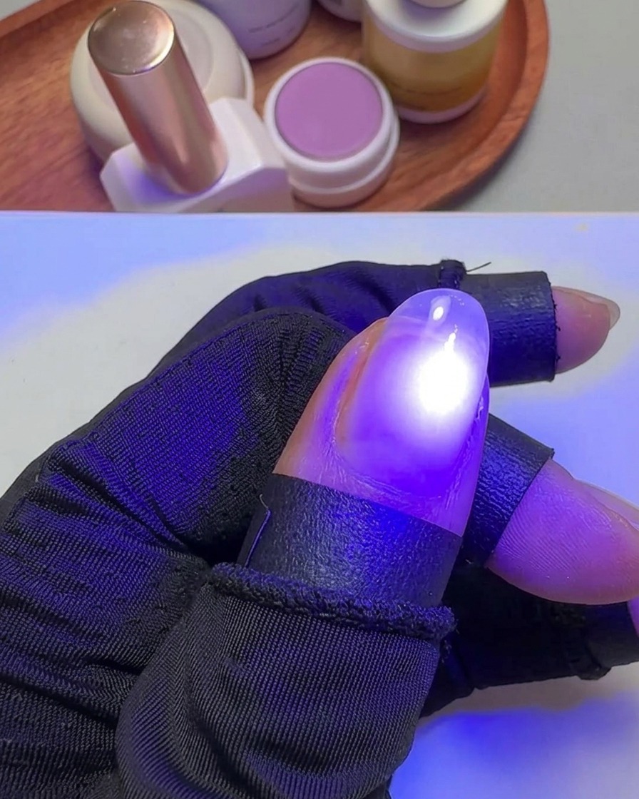 Une main tenant un pouce sous une petite lampe UV violette ciblée pour catalyser le gel.