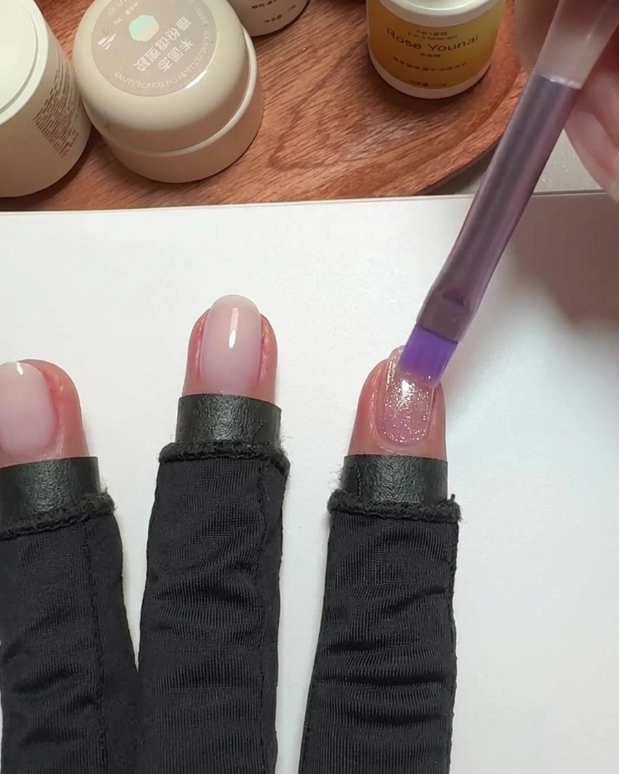 Un pinceau appliquant du vernis cat-eye rose sur un ongle.