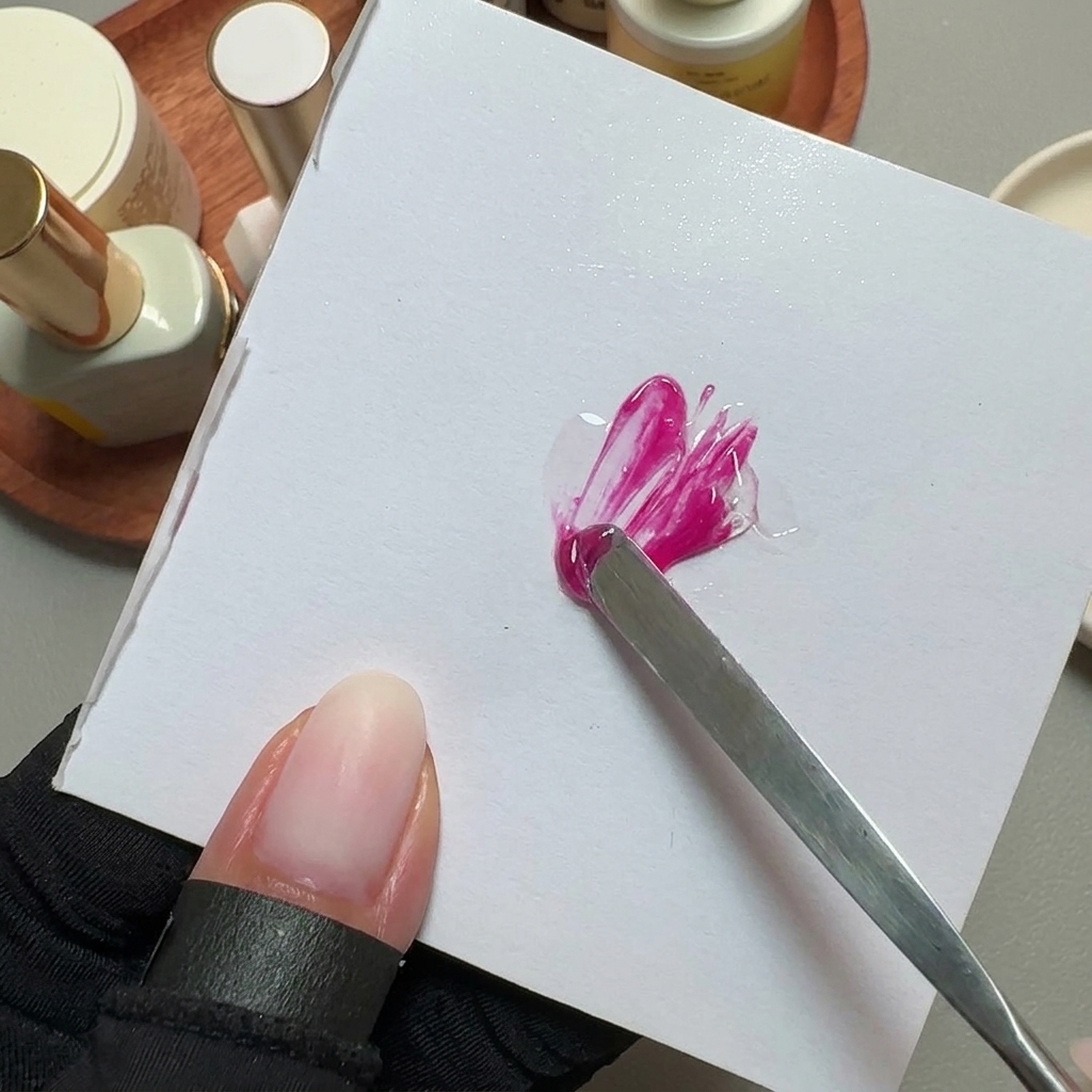 Une spatule en métal mélangeant du vernis gel rose vif sur une palette carrée blanche.