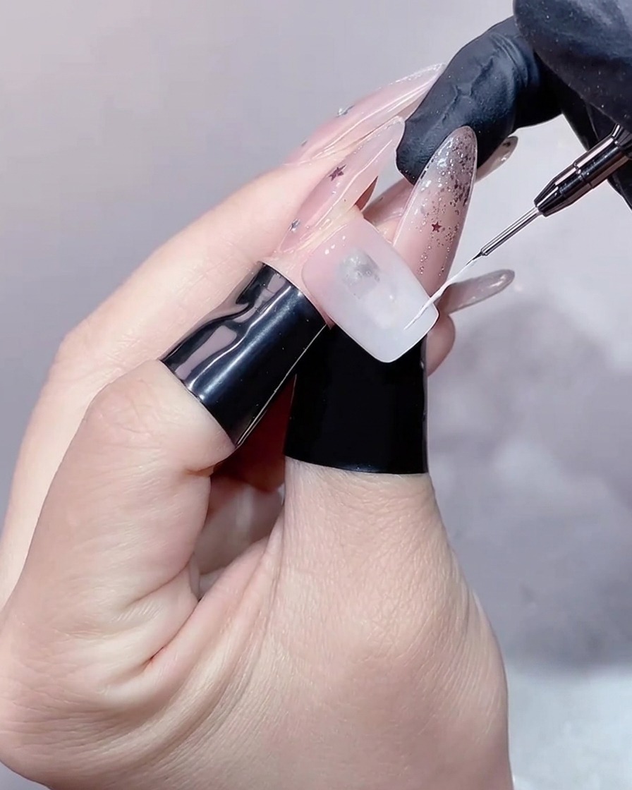 Gros plan dun pinceau liner fin traçant une ligne blanche délicate sur la pointe dun ongle pour créer le contour dune French.