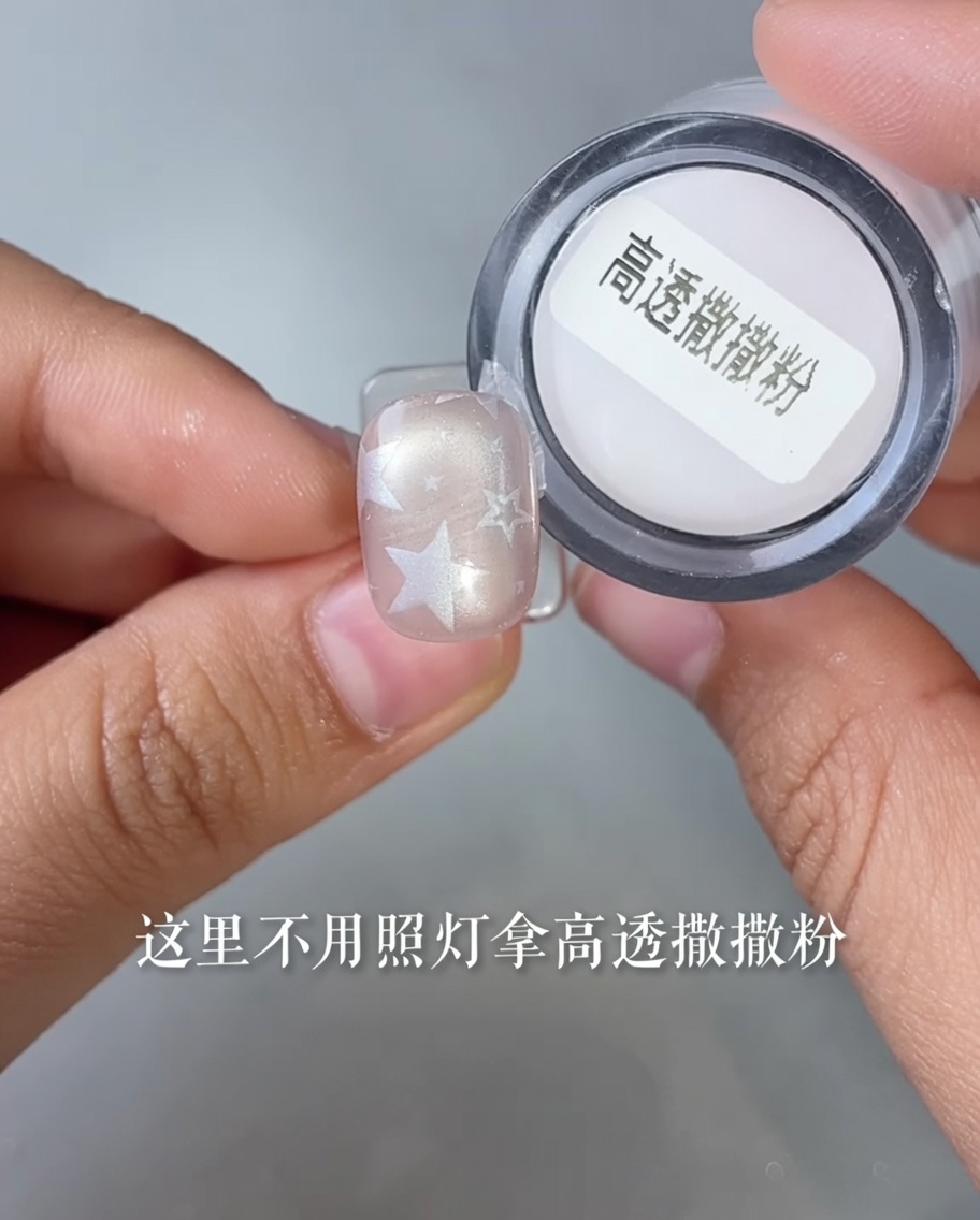 Gros plan dun ongle avec un motif détoile plongé dans un pot de poudre translucide.