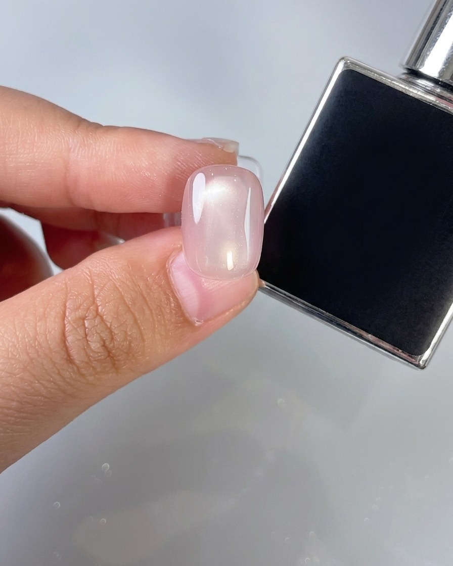 Application dune fine couche de top coat transparent sur un ongle rose.