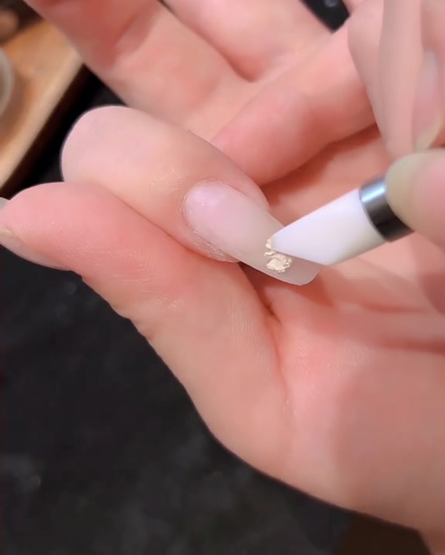 Un pinceau à gel polish appliquant une couche de gel blanc laiteux sur un ongle naturel.