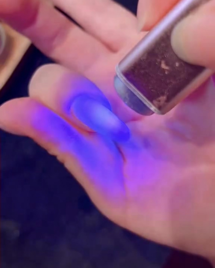 Un pinceau appliquant une couche de gel blanc avec des paillettes effet diamant sur un ongle.