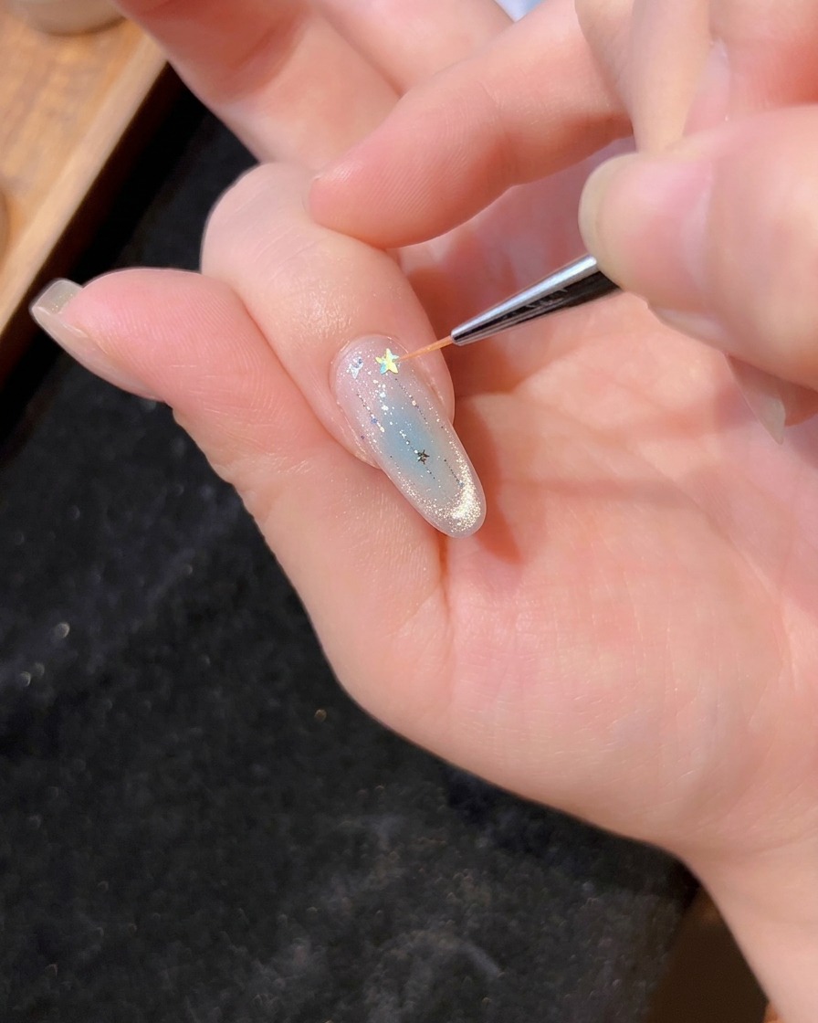 Un pinceau fin plaçant une paillette étoile holographique sur le gel humide dun ongle manucuré.