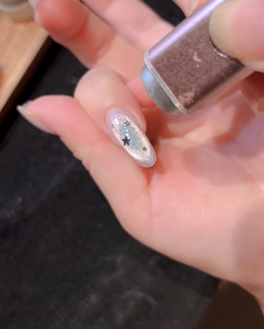 Une lampe UV portable catalysant longle décoré avec des lignes argentées et des paillettes étoiles.