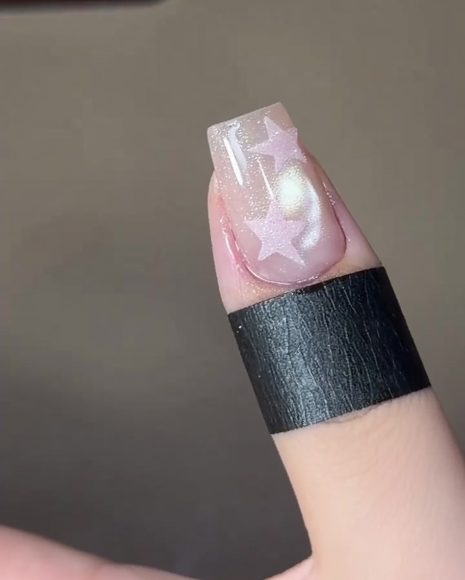 Une pince déposant un sticker stencil en forme détoile sur un ongle manucuré.