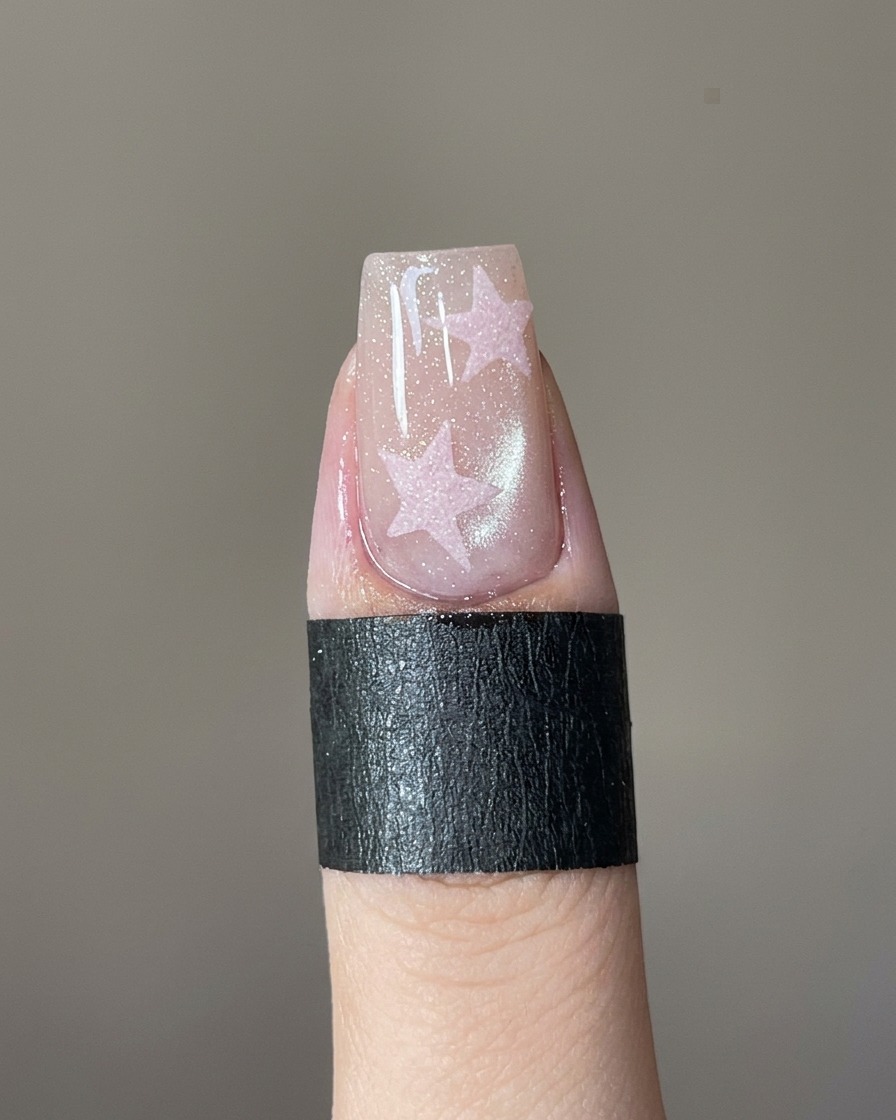 Un pinceau de précision remplissant un stencil étoile sur un ongle avec du gel rose.