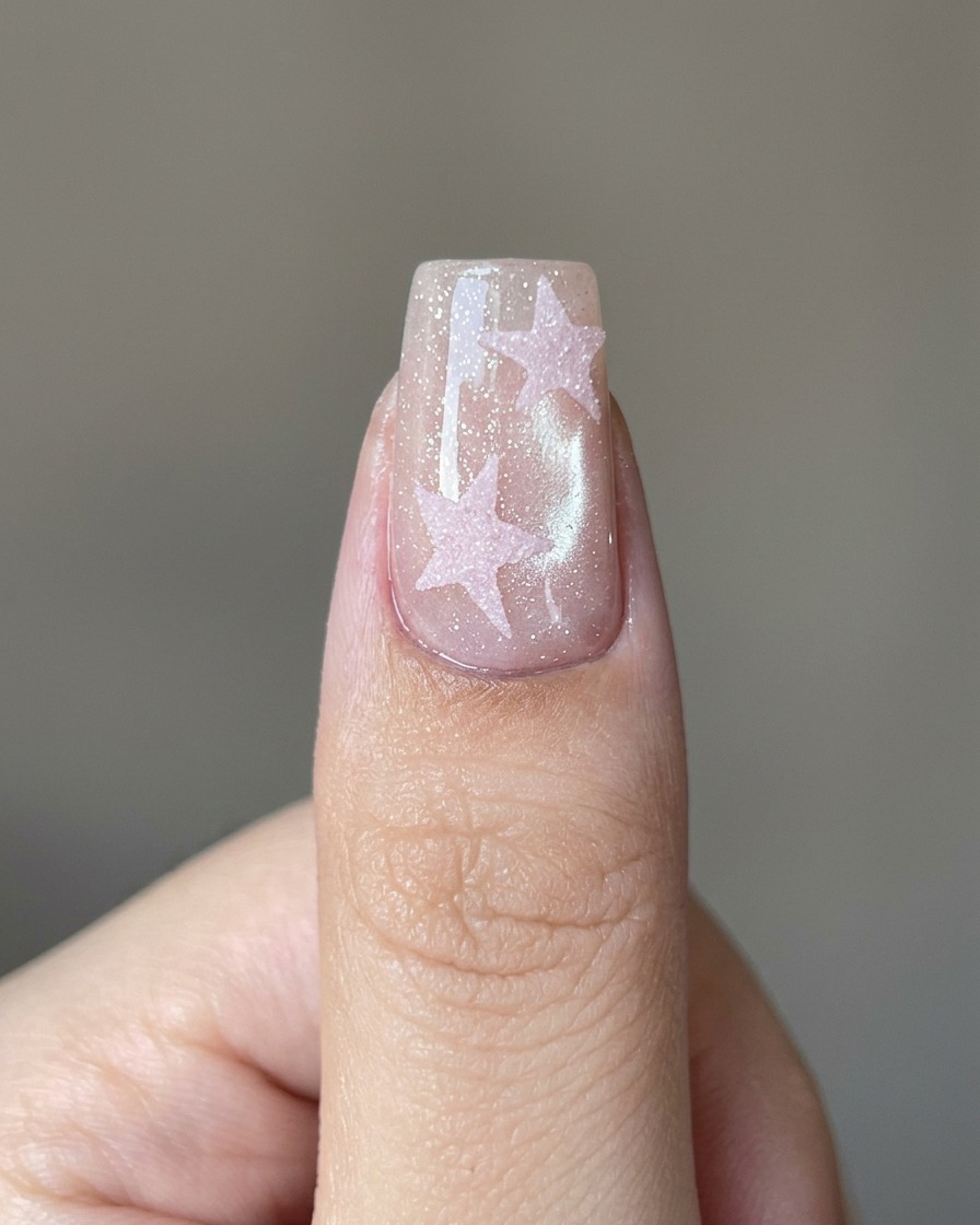 Un pinceau appliquant un top coat transparent sur un design détoile rose sur un ongle.