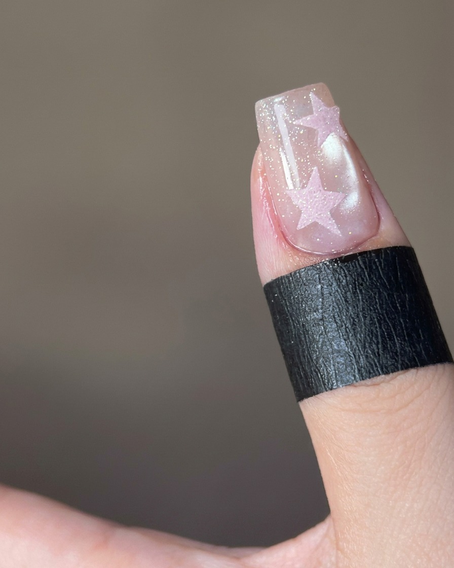 Gros plan montrant de la poudre sugar rose saupoudrée sur un design détoile sur un ongle.