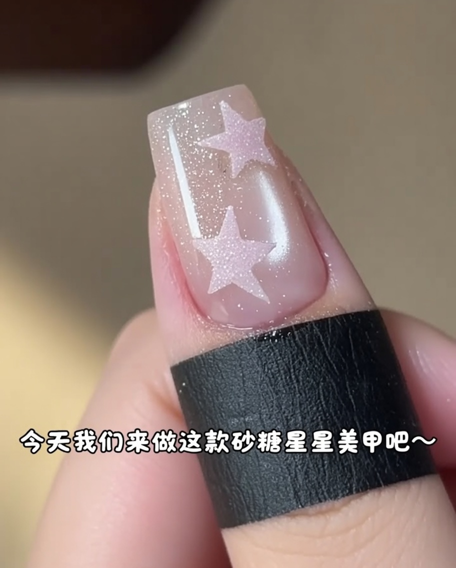 Un petit pinceau appliquant du gel rose dans un sticker étoile sur un ongle.
