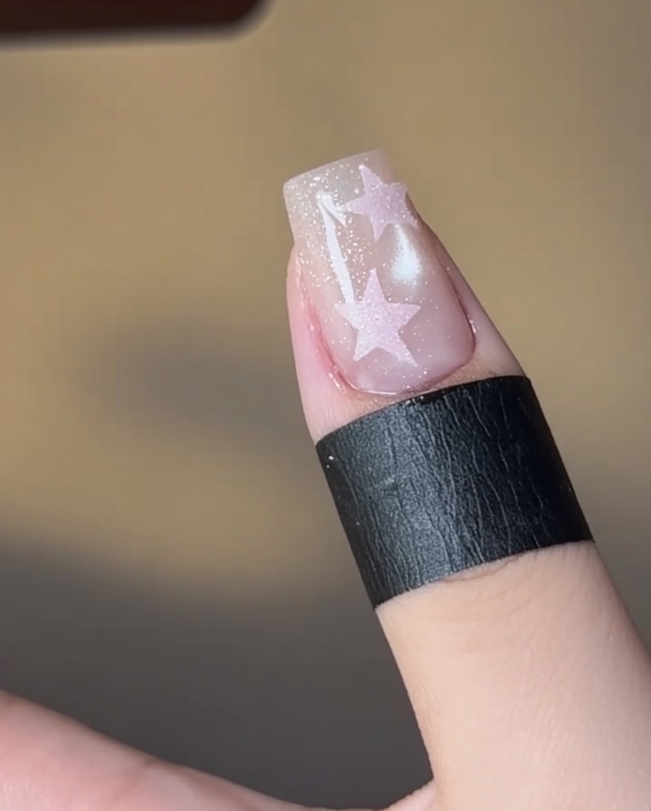 Un ongle avec une étoile remplie de rose en cours de catalysation sous une lampe.