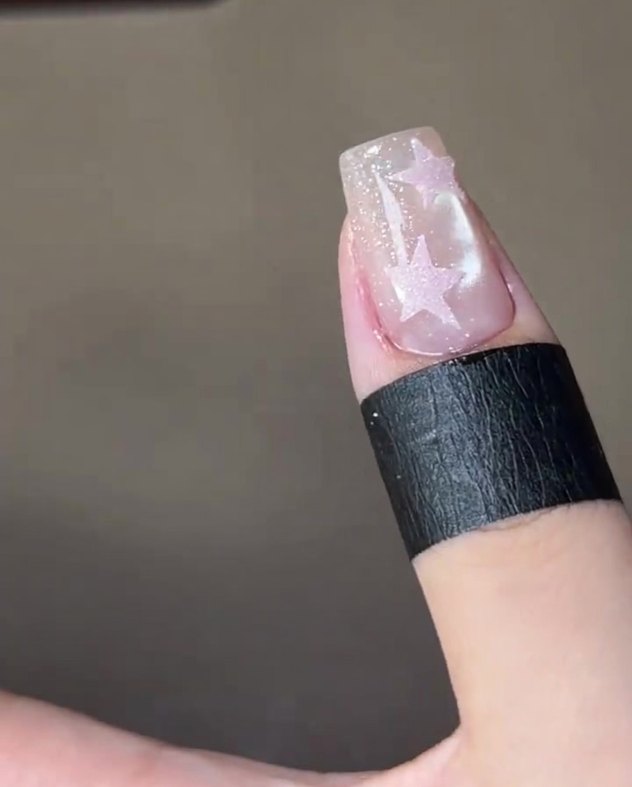 Gros plan dun pinceau appliquant un top coat brillant sur une étoile rose sur un ongle scintillant.