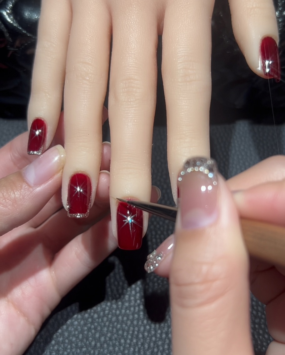 Gros plan dun pinceau liner traçant une ligne fine de paillettes or rose autour du bord dun ongle rouge.