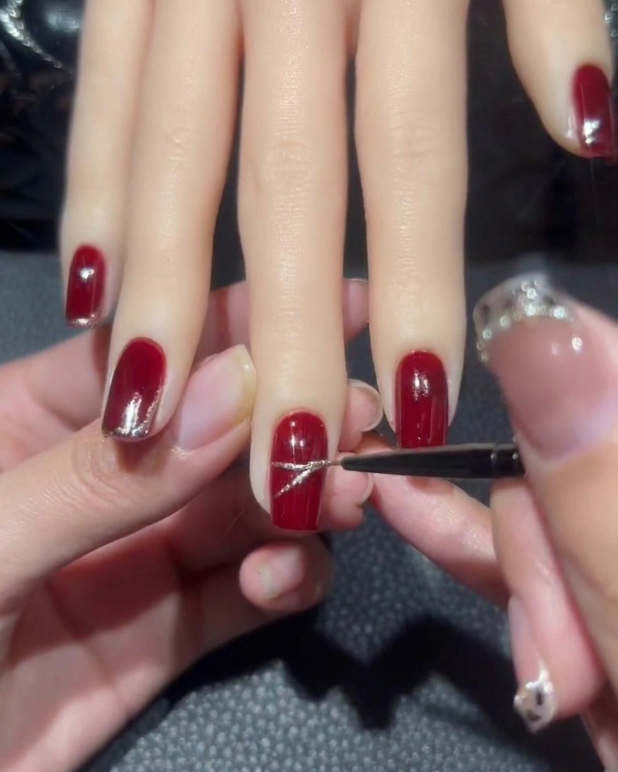 Plan détaillé montrant un X en paillettes or rose dessiné au centre dun ongle rouge.