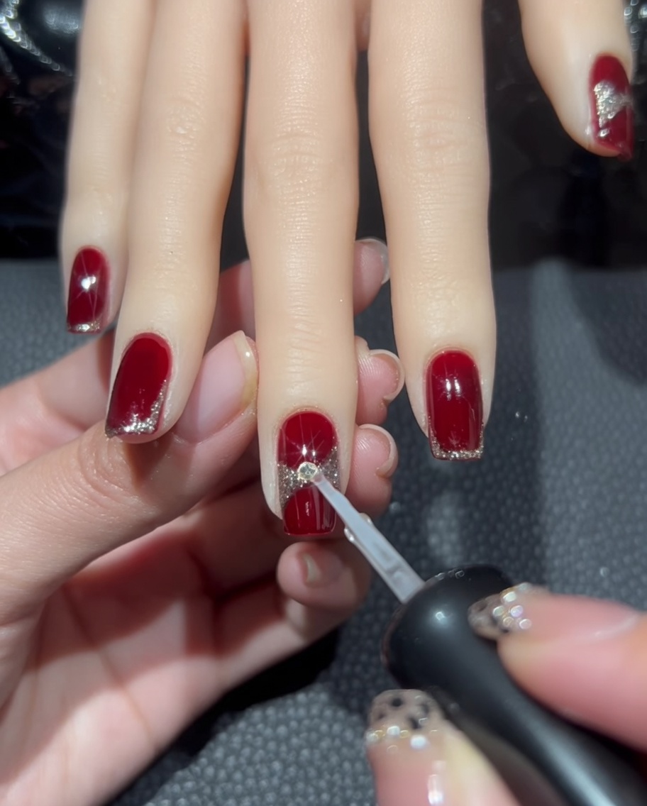 Une goutte de colle à ongles transparente déposée au centre du design de ruban pailleté sur longle.