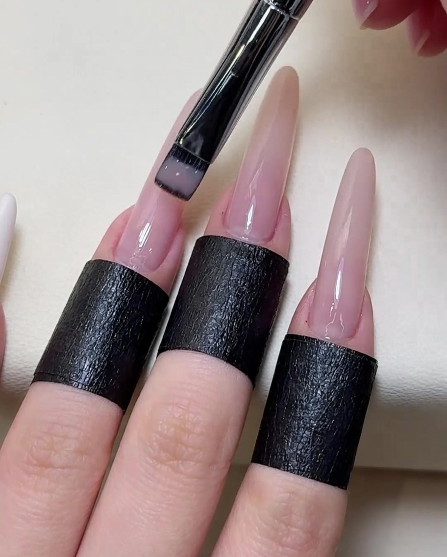 Gros plan sur un pinceau appliquant un vernis gel nude transparent sur toute la surface de longle.