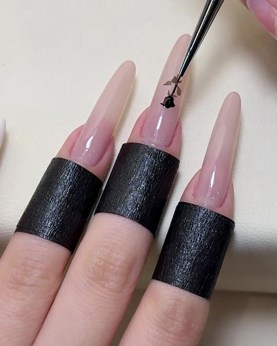 Un pinceau de précision traçant et remplissant les détails dune rose blanche avec du vernis gel noir.