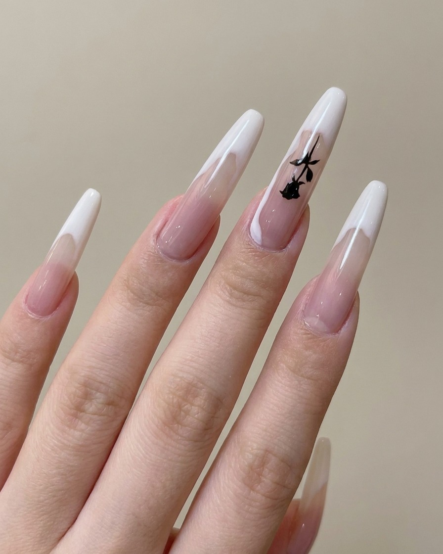 Gros plan dun pinceau dessinant un motif de branche noire fine sur un ongle déjà doté dune French manucure.