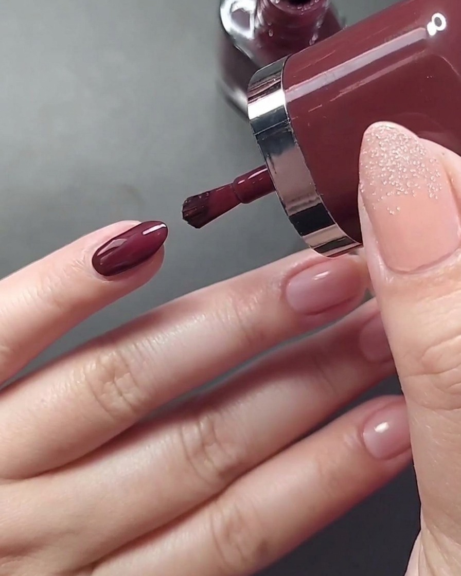 Gros plan sur lapplication dun vernis beige nude sur longle de lannulaire.