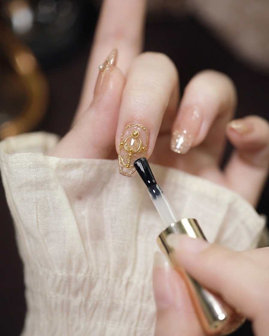 Un pinceau à gel transparent appliquant une couche protectrice sur un ongle décoré avec du chrome et des perles.