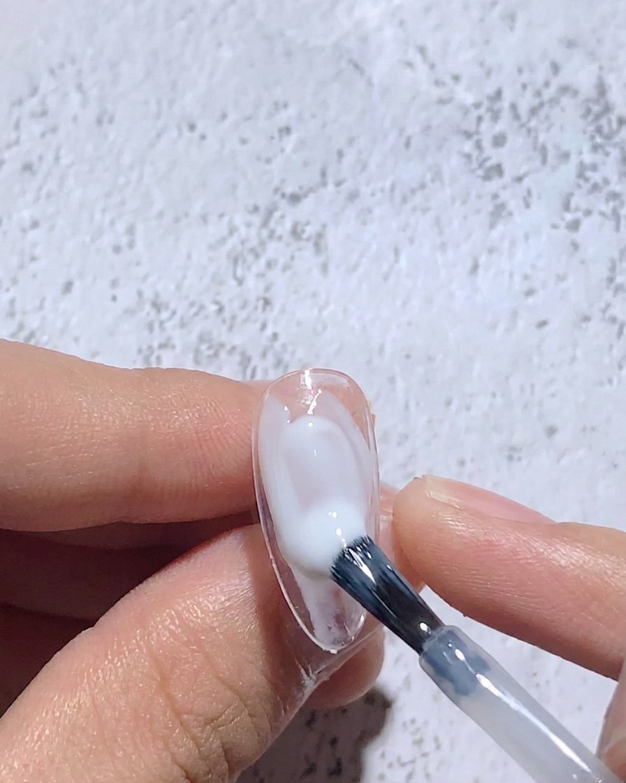 Un pinceau fin estompant le gel blanc humide sur une capsule pour créer un centre flou.