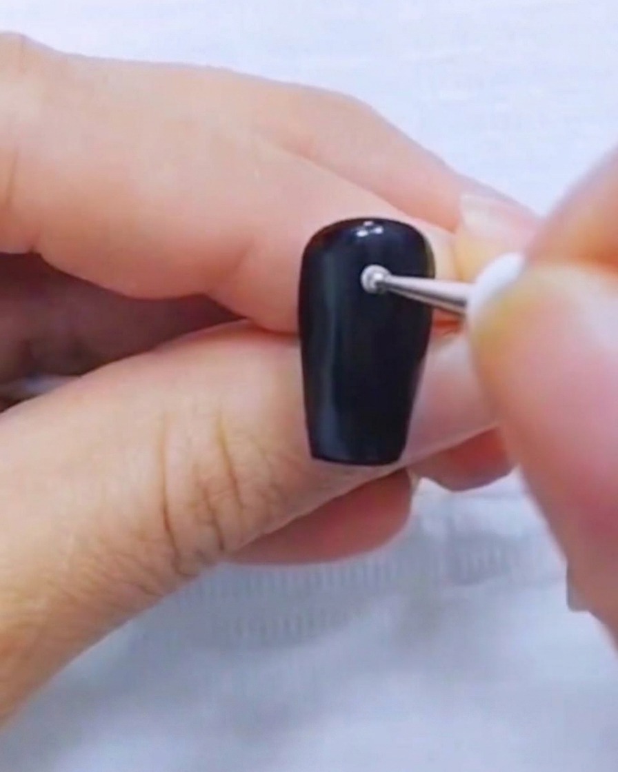 Gros plan dun dotting tool plaquant un petit point blanc sur un ongle noir.