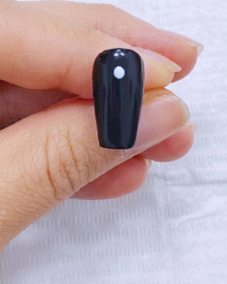 Un ongle noir avec un point central et quatre points disposés en cercle autour.