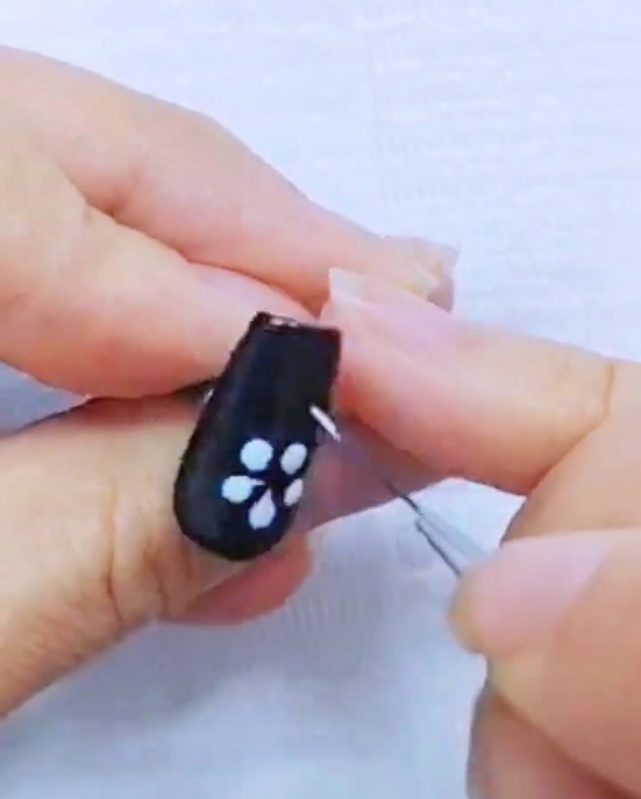 Gros plan dun pinceau liner affinant les pétales en gel blanc sur longle noir.