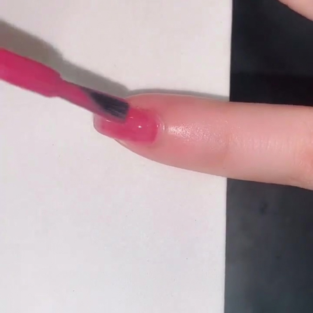 Un pinceau de vernis à ongles ajoutant une troisième couche de gel jelly rose pour intensifier la couleur sur longle.