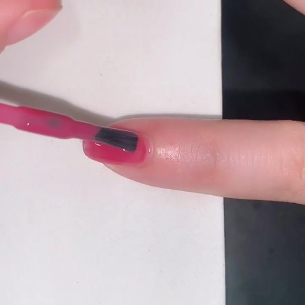 Un pinceau appliquant un vernis jelly rose translucide sur un ongle.